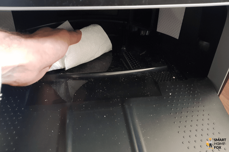 The floor of the wiping station is cleaned with a paper towel.